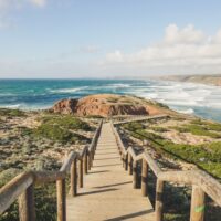 a sandy beach with blue sea ahead and a wooden boardwalk stretching away